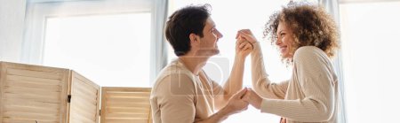 Preciosa pareja joven pasar tiempo juntos en casa bailando cogidos de la mano con sonrisa, pancarta