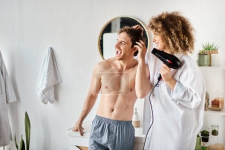 Photo for Man shouting while his girlfriend is drying his hair with hairdryer in the morning, bonding couple - Royalty Free Image