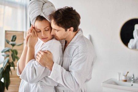 Téléchargez les photos : Jeune couple amoureux en peignoirs dans la salle de bain, s'embrassant, homme embrassant sa petite amie - en image libre de droit