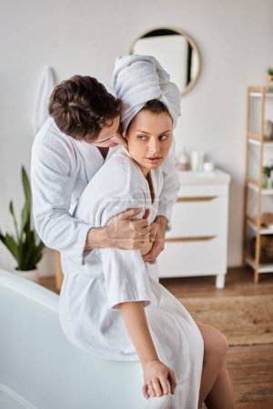 Paar in Bademänteln am Morgen, Mann umarmt und küsst seine Freundin von hinten