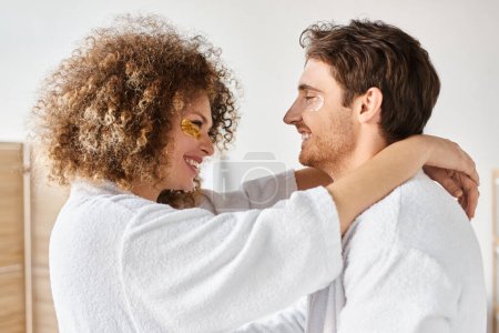 Portrait of happy couple with eye patches  hugging in bathroom and smiling, looking at each other