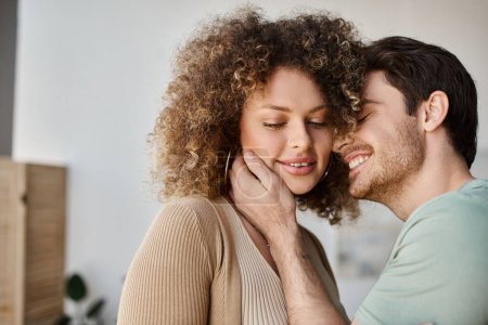 Téléchargez les photos : Couple amoureux de bel homme et femme bouclée à la maison le matin, souriant et étreignant - en image libre de droit