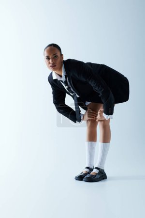 Young African American woman stands on one leg in suit and tie in a studio setting, balance.