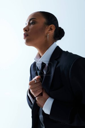 A young African American woman dressed in suit, gazes into distance with contemplative expression.