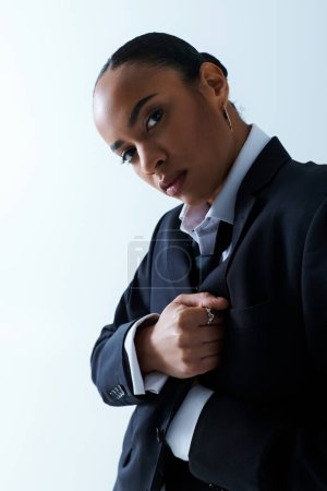 Foto de Joven mujer afroamericana de 20 años ajustando su corbata en un ambiente de estudio. - Imagen libre de derechos
