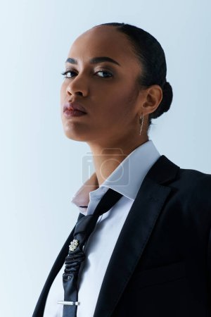 Photo for Young African American woman wearing a suit and tie, gazes off to the side in a studio setting. - Royalty Free Image