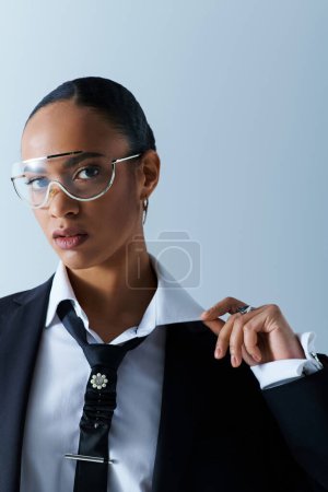 Junge Afroamerikanerin in ihren Zwanzigern, in Anzug und Krawatte, mit Brille selbstbewusst.