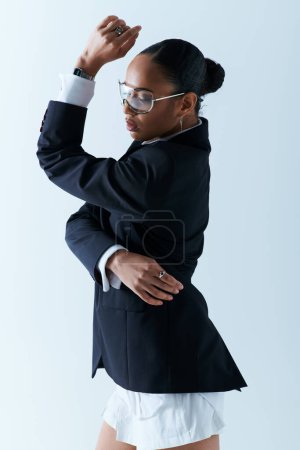 Young African American woman dressed in a suit and glasses, striking a pose in studio