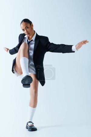 A young black corporate woman in a suit and tie energetically kicks in studio