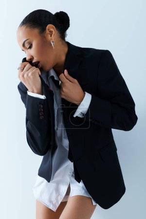 A young African American woman exudes confidence in tailored suit and tie in a studio.