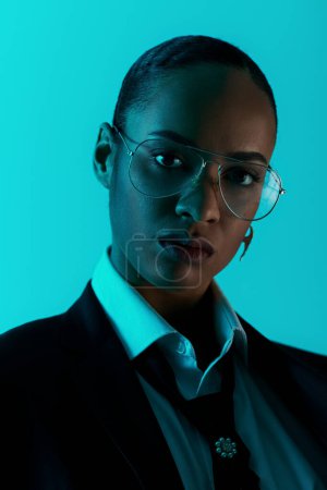 A young African American woman confidently posing in sharp suit and stylish glasses