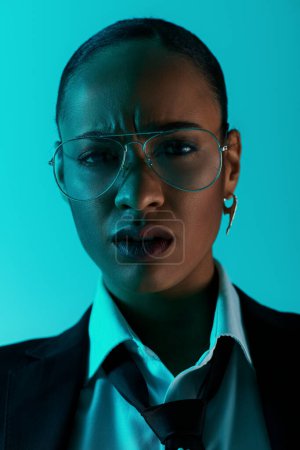stylish African American woman confidently wears a suit and tie, accessorized with glasses