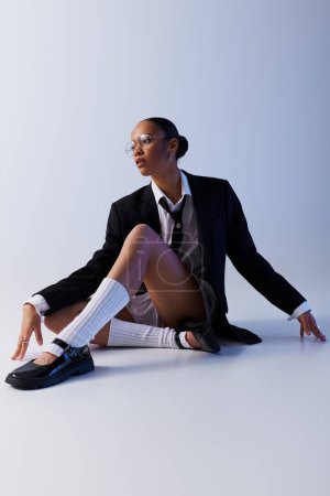Photo for A stylish young African American woman in a suit and tie sits confidently on the floor. - Royalty Free Image
