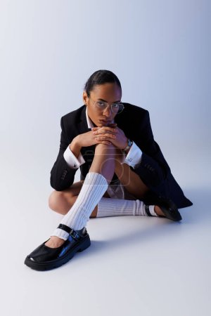 Joven mujer afroamericana sentada con las piernas cruzadas en el suelo en una pose pacífica en el estudio