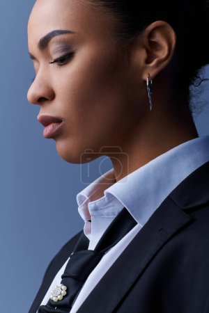Photo for Young African American woman in suit and earrings gazes into the distance. - Royalty Free Image