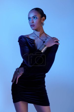 A young African American woman strikes a pose in a black dress for a glamorous portrait.