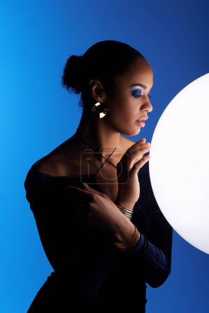 A young African American woman gracefully holds a large white ball in her hands in a studio setting.