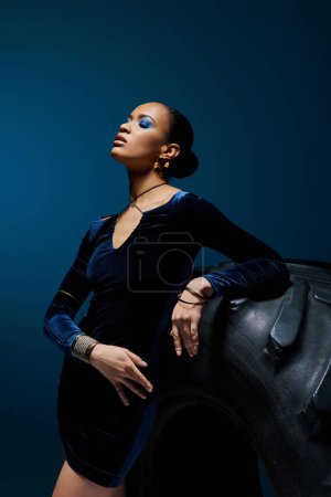 Eine junge Afroamerikanerin steht neben einer hoch aufragenden schwarzen Tasche in einem Studio-Setting.