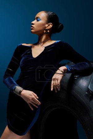 African American woman in black dress leaning gracefully against a tire.