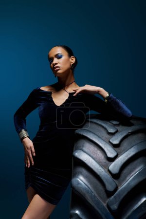 A young African American woman with a determined expression standing confidently next to a giant tire.