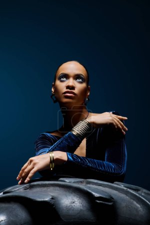A young African American woman gracefully seated on top of a sleek black object in a studio setting.