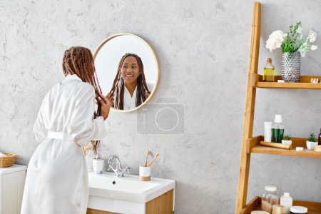 An African American woman with afro braids stands in her modern bathroom, admiring her reflection in the mirror.