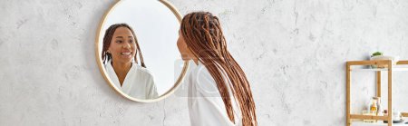Eine afroamerikanische Frau mit Afro-Zöpfen betrachtet ihr Spiegelbild im Spiegel eines modernen Badezimmers und betrachtet Schönheit und Hygiene.