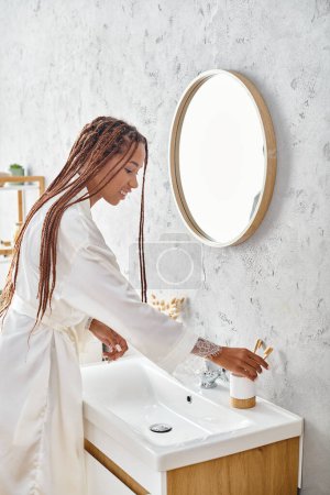 Photo for An African American woman with afro braids washes her hands in a modern bathroom, practicing personal hygiene and self-care. - Royalty Free Image