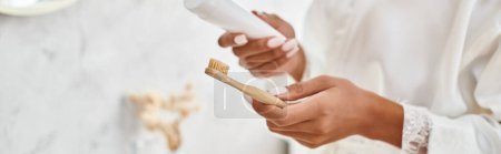 Photo for A close-up of an African American woman with Afro braids holding a toothbrush in her modern bathroom. - Royalty Free Image