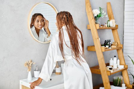 Eine afroamerikanische Frau mit Afro-Zöpfen steht in einem modernen Badezimmer und bürstet ihre Haare vor einem Spiegel.