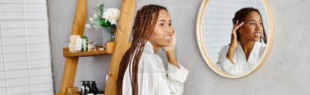 Une Afro-Américaine avec des tresses afro se tient devant un miroir, se brossant les cheveux dans une salle de bain moderne.