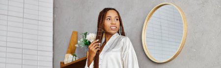 An African American woman with dreadlocks stands in front of a mirror in a modern bathroom, admiring her appearance.