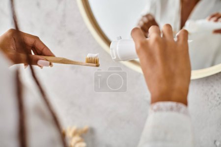 Una mujer afroamericana en un albornoz cepillándose los dientes en un baño moderno.