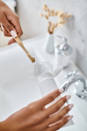 An African American woman in a bathrobe brushes her teeth in a modern bathroom.