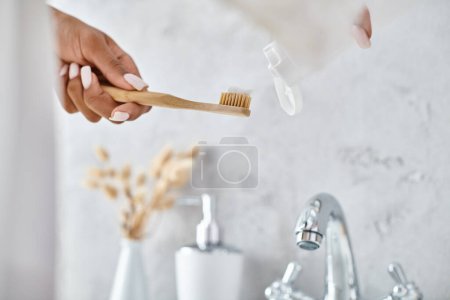 African American woman in bathrobe holding toothbrush in modern bathroom, emphasizing beauty and hygiene routine.