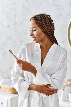 Une femme afro-américaine en robe blanche tient délicatement un pinceau, exsudant créativité et grâce dans un cadre de salle de bain moderne.