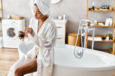 Téléchargez les photos : Une Afro-Américaine s'assoit paisiblement sur une baignoire dans une salle de bain moderne tout en portant un peignoir. - en image libre de droit