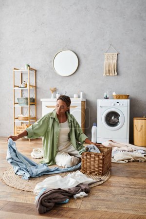 Eine Frau mit Afro-Zöpfen sitzt auf dem Boden vor einer Waschmaschine und wäscht ihre Wäsche im Badezimmer.