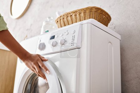 Woman putting a cloth into the dryer in a bathroom while doing laundry.
