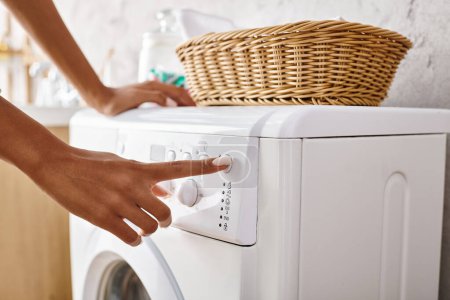 African American woman with afro braids pushing button on washing machine doing laundry in bathroom.