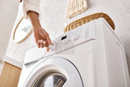 Téléchargez les photos : Une Afro-Américaine appuyant sur un bouton sur une machine à laver dans une salle de bain, faisant la lessive. - en image libre de droit