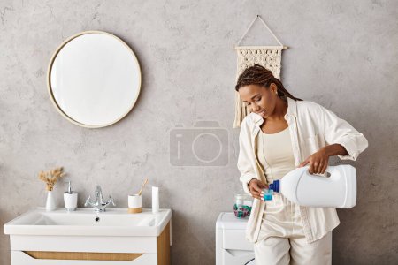 Eine afroamerikanische Frau mit Afro-Zöpfen gießt friedlich Waschmittel in einen Behälter, während sie im Badezimmer Wäsche wäscht.