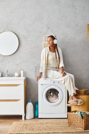 Eine afroamerikanische Frau mit Afro-Zöpfen sitzt auf einer Waschmaschine und macht einen Moment der Ruhe während ihrer Wäsche-Routine.