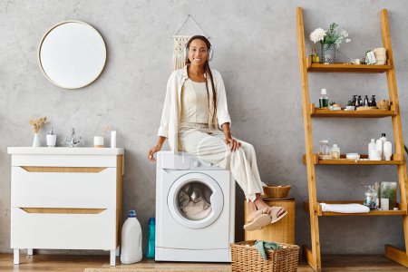 An African American woman with afro braids sits confidently on a washing machine doing laundry in a bathroom.
