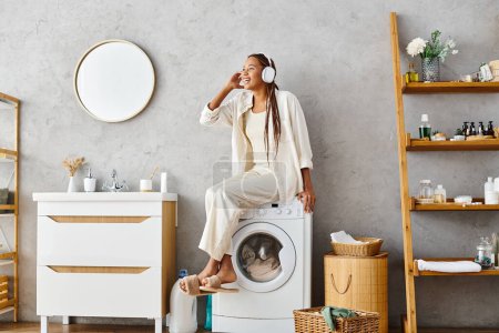 African American woman with afro braids doing laundry, sitting atop a washing machine in a bathroom.