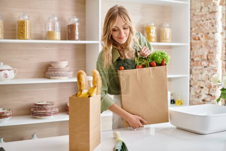 A woman carrying a full grocery bag of fresh produce in her apartment kitchen.