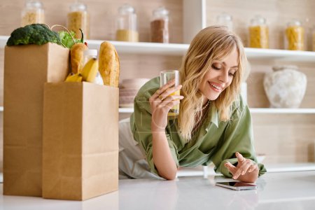 Téléchargez les photos : Une femme assise à une table dans une cuisine, concentrée sur son téléphone portable. - en image libre de droit