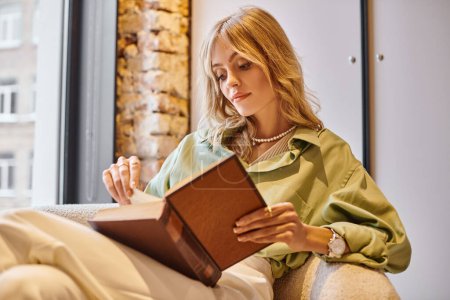 Une femme assise sur un canapé absorbé dans un livre dans un appartement confortable.