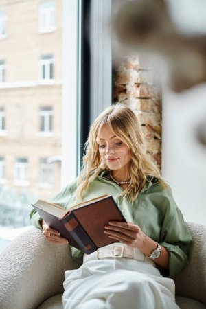 Una mujer sentada en una silla en casa, absorta en leer un libro.