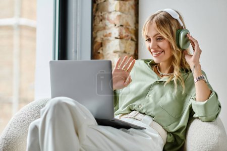 A woman in a chair working on a laptop with headphones on.